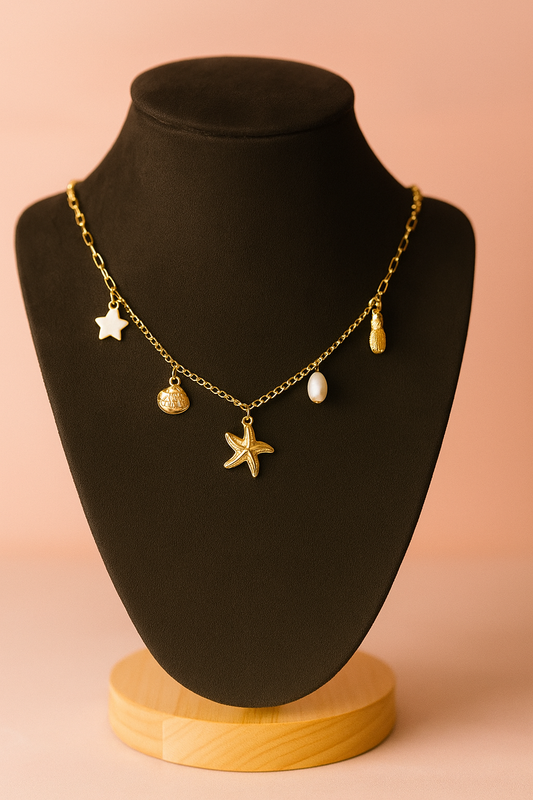 Gold necklace with starfish and beach charms- starfish,pineapple,stars , coin and pearl on a black mannequin bust against a pink background