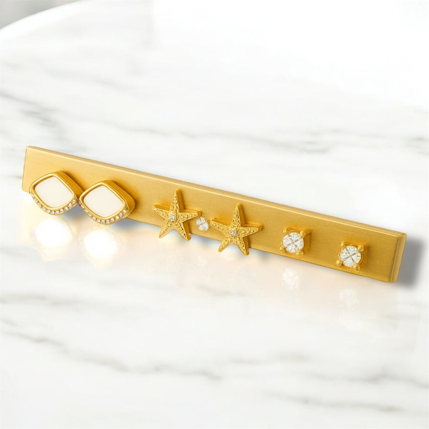 Set of 3 pairs of earrings with starfish and circular designs on a white fabric background