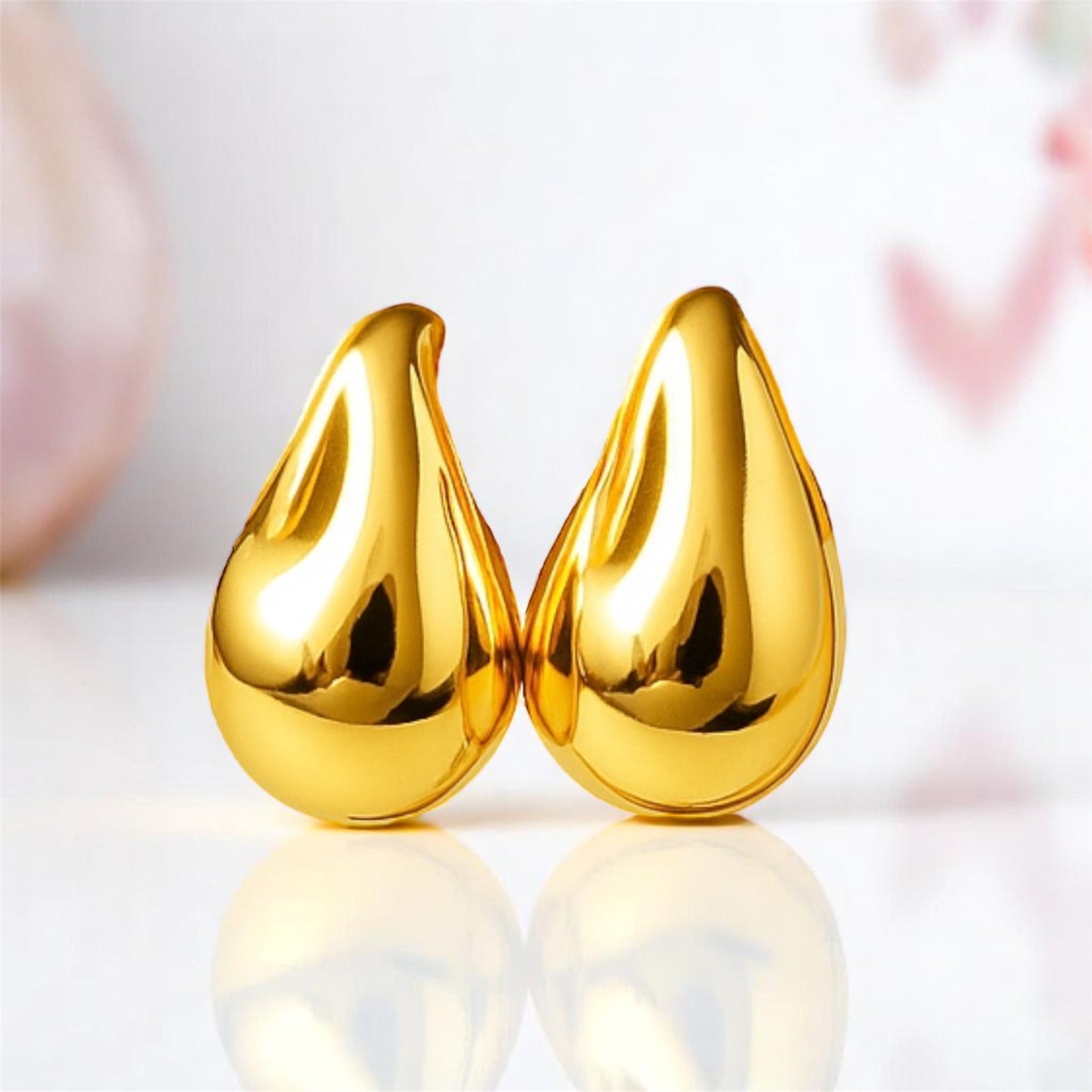 Pair of gold teardrop-shaped earrings on a reflective surface with a blurred background