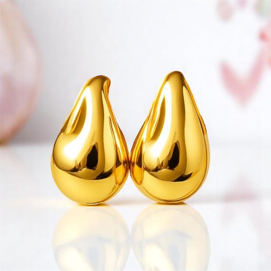 Pair of gold teardrop-shaped earrings on a reflective surface with a blurred background