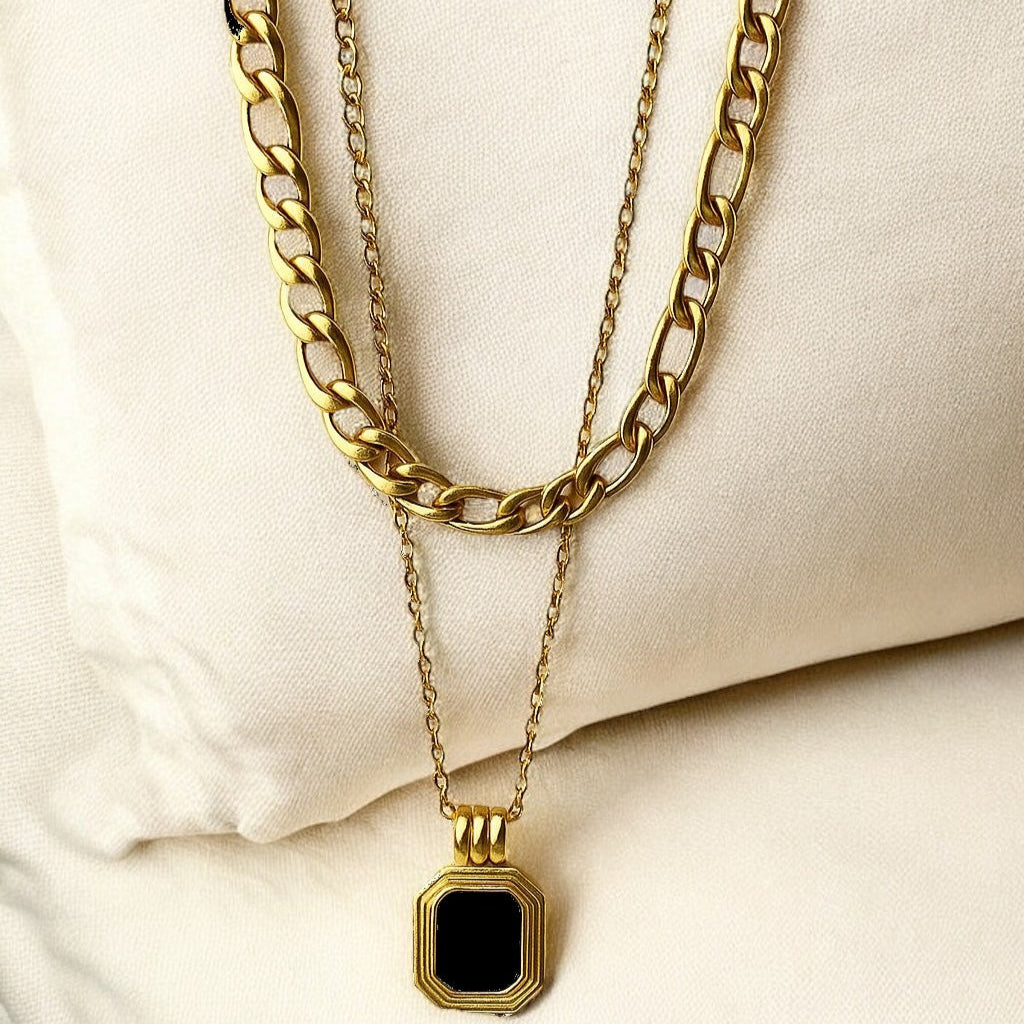 Two gold necklaces with a black pendant on a beige surface
