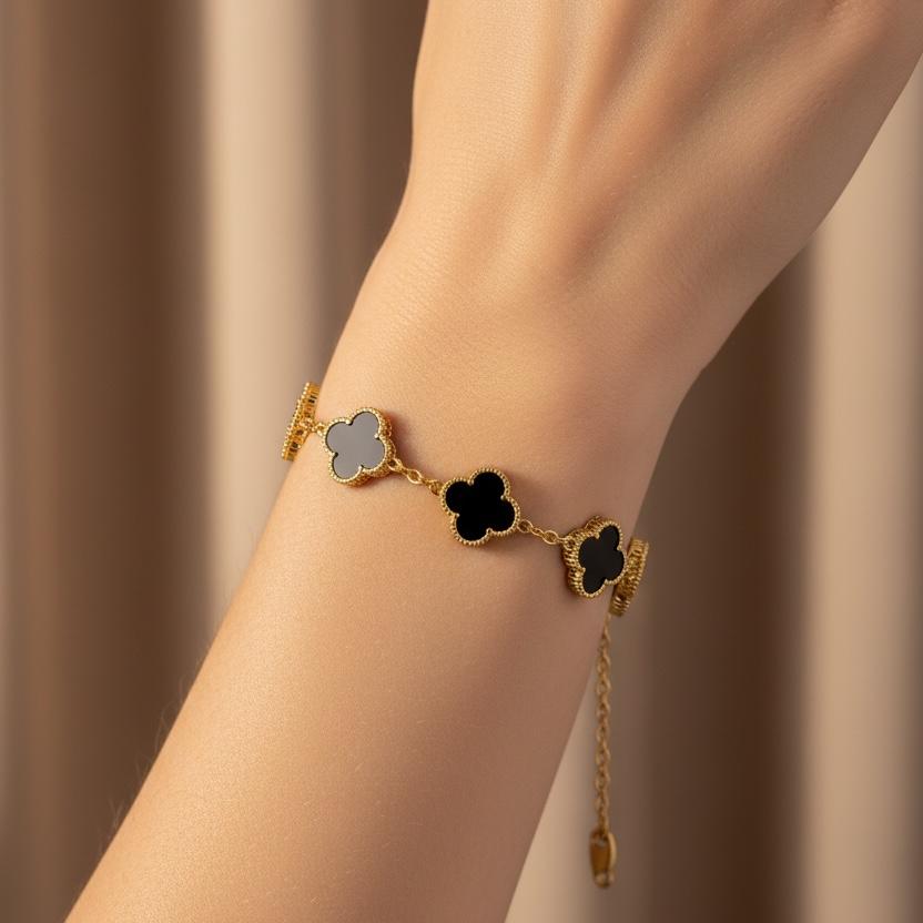 Gold bracelet with black clover-shaped charms on a wrist against a neutral background
