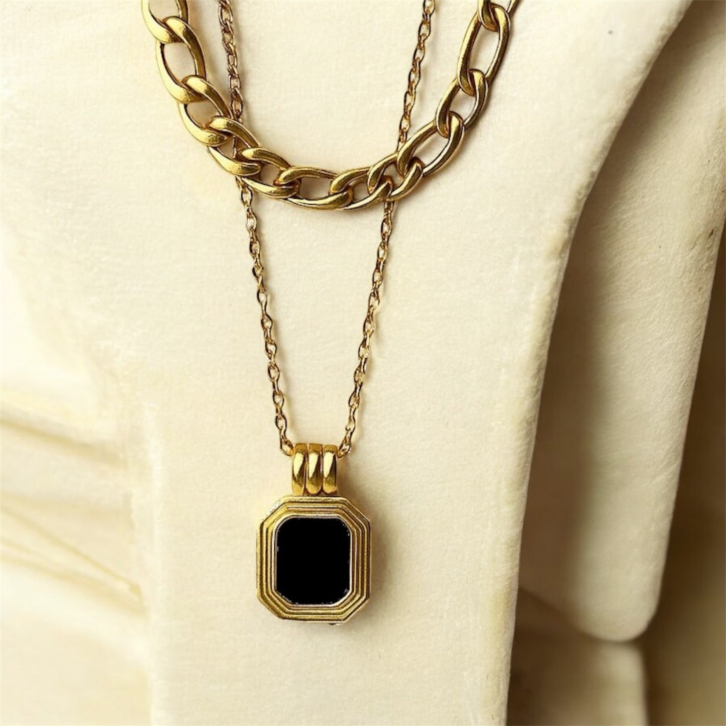 Gold necklace with a black pendant on a beige surface