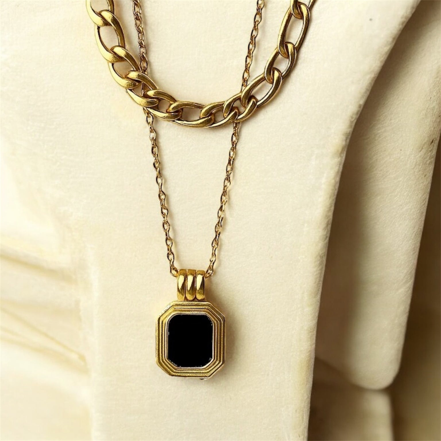 Gold necklace with a black pendant on a beige surface
