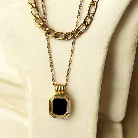 Gold necklace with a black pendant on a beige surface