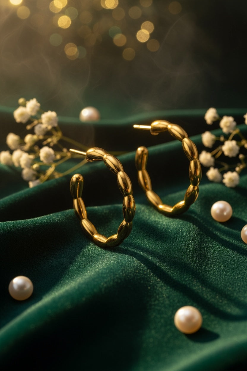 Gold hoop earrings on a green fabric background with small white flowers and pearls.